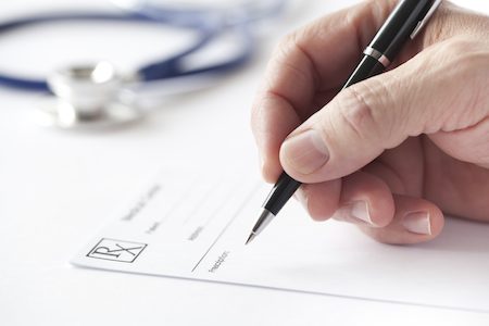 Photo of hand with pen writing on prescription pad