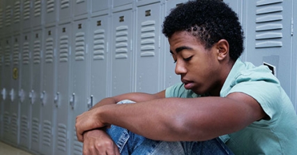  Muchacho adolescente sentado contra los casilleros pensando.