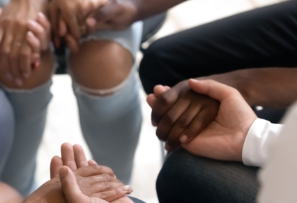 Diversas personas sentadas en círculo cogidas de la mano en terapia de grupo
