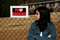 Teen girl leaning against a metal fence that has a sign stating No Smoking