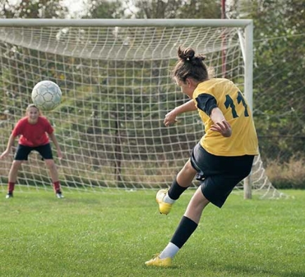  Dos niñas jugando al fútbol. Una niña patea una pelota hacia la red.